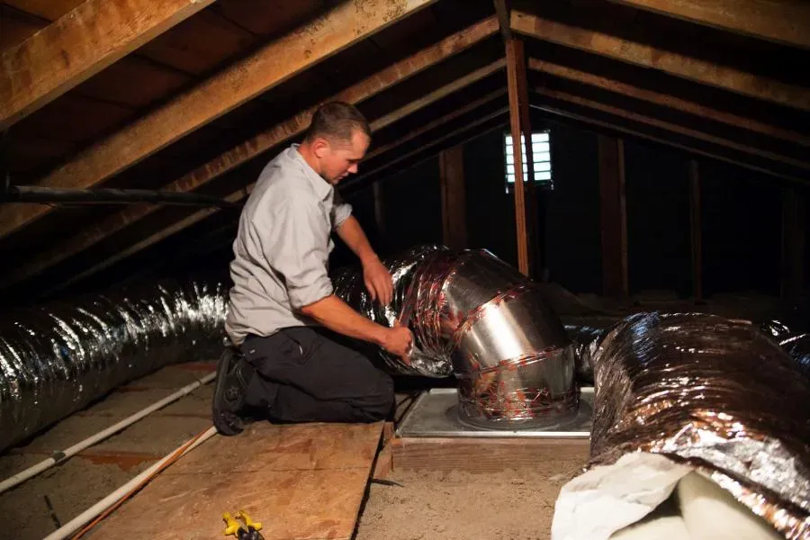 A technician from Moore Home Services working on ductwork installation in an attic, surrounded by insulated ducts, highlighting professional HVAC services in Brea.